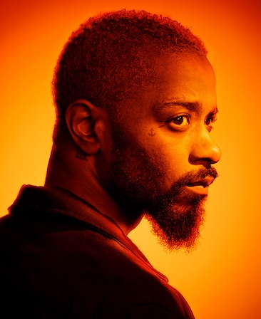 Headshot of LaKeith Stanfield looking over his shoulder with heavy orange sunset lighting over face and background
