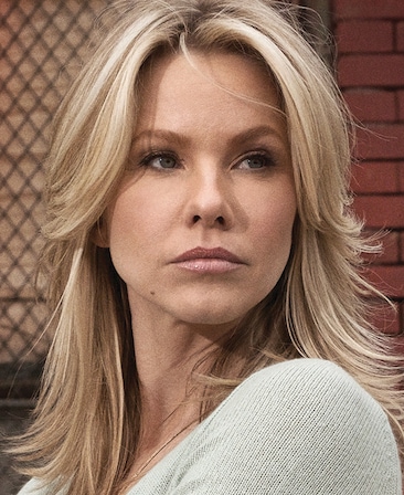 Andrea Roth headshot wearing a gray shirt and standing outside in front of a brick wall