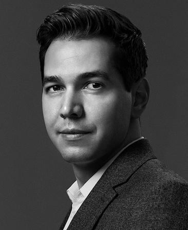 Black and white headshot of Executive Producer Tanase Popa of FX's Love Story, wearing a textured suit and button on.