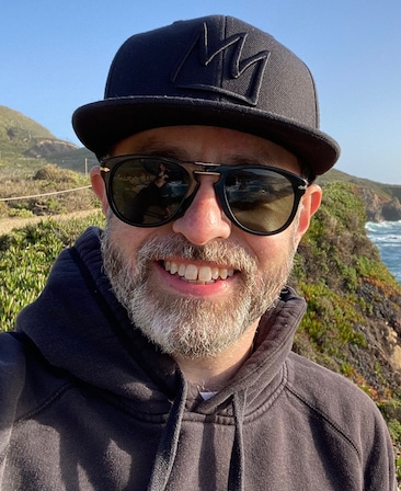 Headshot of Andy Thomas wearing a black baseball cap and sunglasses