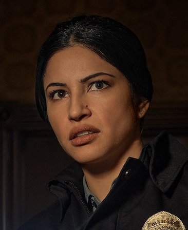 Richa Moorjani headshot wearing a jacket with a police badge on the front