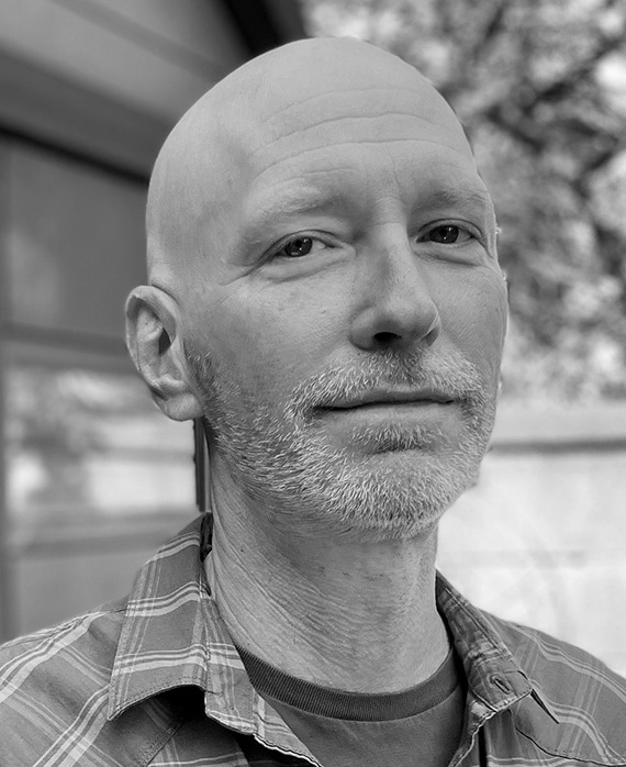 Taylor Elmore headshot standing outside, wearing a plaid shirt.