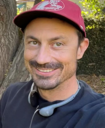 Rob Rosell headshot standing outside wearing a red baseball cap and gray headphone around neck 