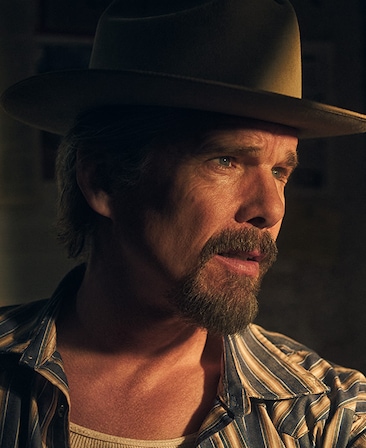 Headshot of Ethan Hawke as Lee Raybon in FX's The Lowdown, wearing a striped top and tan fedora, with golden light on him.