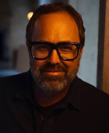 Headshot of executive producer Scott Robertson of FX's Love Story, wearing a black polo and black framed glasses.