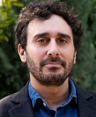 Jake DeVito headshot standing outside and wearing a blue shirt with a navy jacket over