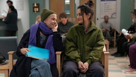 Molly and Nikki sitting in a waiting room looking at each other and smiling. 