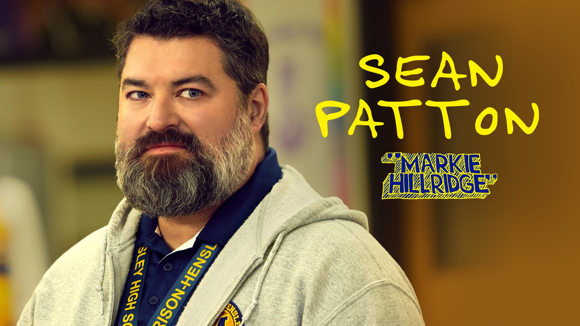 Sean Patton as Markie Hillridge for FX's English Teacher wearing a grey zip-up hoodie and blue collared shirt.