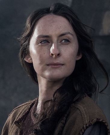 Sarah Sweeney headshot in layered brown ancient peasant clothing with hair braided in side ponytail