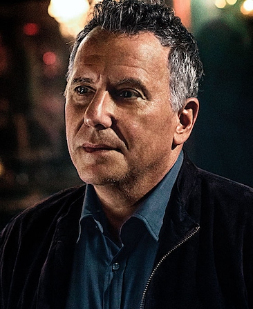 Paul Reiser headshot wearing a blue button up shirt and black jacket