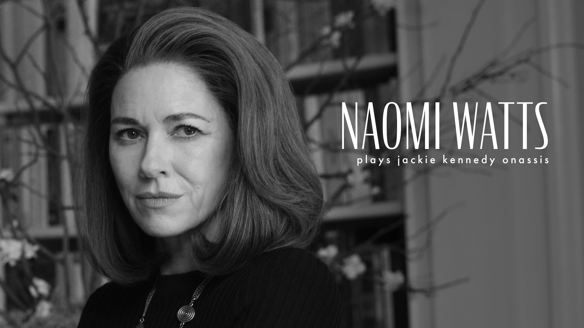 Headshot of Naomi Watts as Jackie Kennedy in FX's Love Story in a black sweater and long necklace.