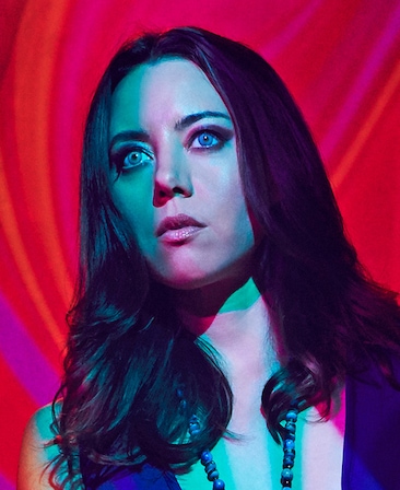 Aubrey Plaza as Lenny in FX's Legion, with blue eye contacts, blue dress, with red hallucinogenic background 