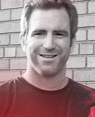 Even Reilly headshot wearing black shirt standing in front of a brick wall