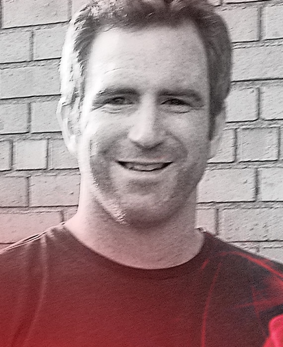 Even Reilly headshot wearing black shirt standing in front of a brick wall