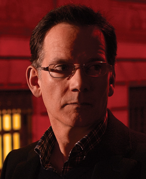 Campbell Scott as Joe Tobin in FX's Damages, in black coat, standing outside with dark red lighting on wall behind him