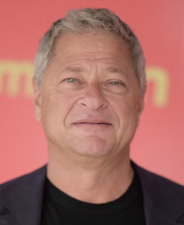 Michael Rotenberg headshot wearing a black shirt and black jacket standing in front of a red sign