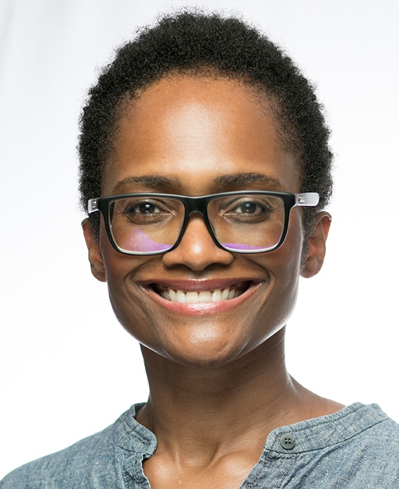 Courtney Lee Mitchell headshot in grey buttoned top and wearing black glasses with plain white background