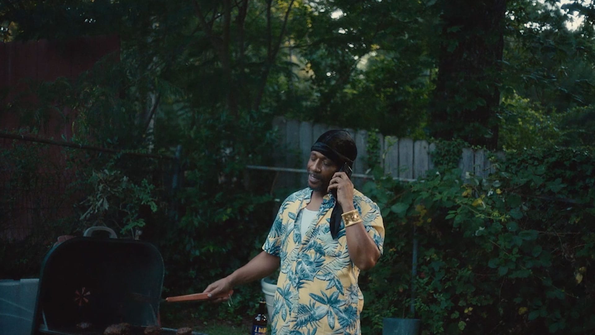 Uncle Willie from Atlanta FX show wearing blue and yellow Hawaiian shirt talking on the phone while grilling outside