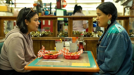 Two women sitting across each other at a dining table in a restaurant with red trays in front of them.