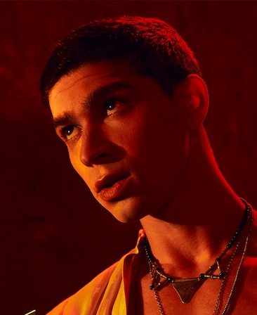 Headshot of Isaac Powell wearing silver necklace under red lighting