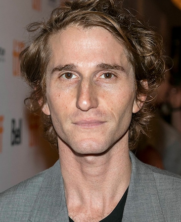 Headshot of executive producer Max Winkler of FX's Love Story, wearing a black shirt and grey suit.