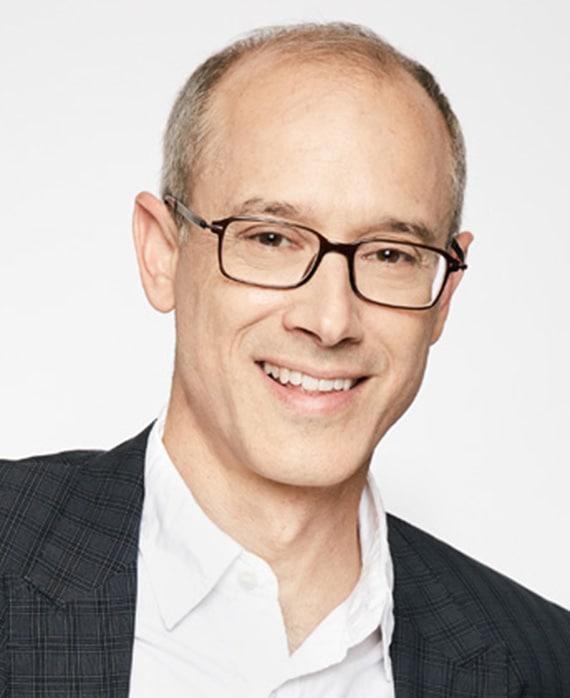 David W. Zucker headshot in dark brown glasses with white button down and black plaid blazer, against plain white background