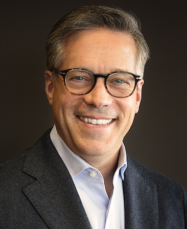 Steve Stark headshot wearing a white button down and black suit jacket with glasses, against a black background