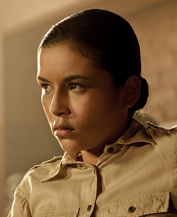 Emily Rios headshot in beige cargo uniform with hair in bun, looking to the side with sun shining on face