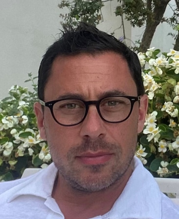Nick Frenkel wearing a white shirt, sitting in front of a flower bush