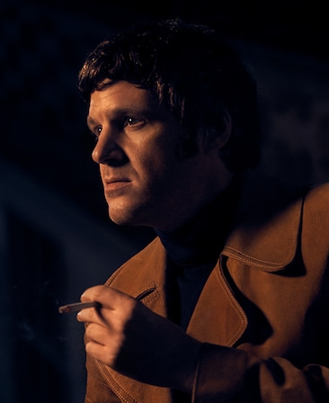 Michael Esper Headshot wearing a brown jacket and holding a cigarette