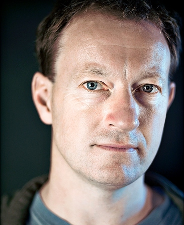Simon Beaufoy Headshot wearing a blue shirt and black jacket