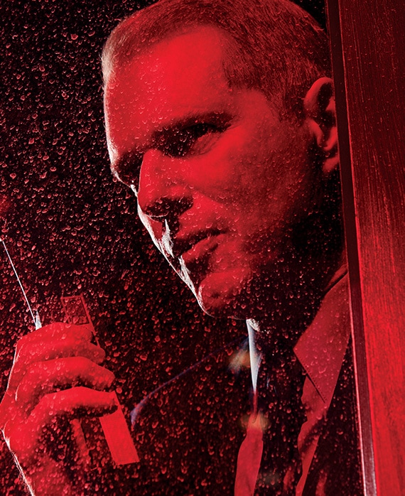 Noah Emmerich headshot holding walkie talkie in hand and looking up behind wet glass under red lighting