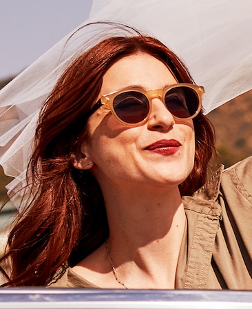 Aya Cash headshot wearing orange sunglasses and khaki top