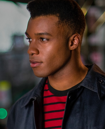 Dyllón Burnside headshot wearing a black and red striped shirt with black jacket over
