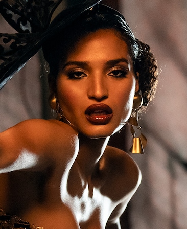 Indya Moore headshot wearing gold earrings and a big black hat
