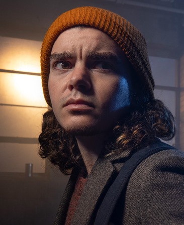 Elliot Fletcher headshot wearing an orange beanie and brown jacket