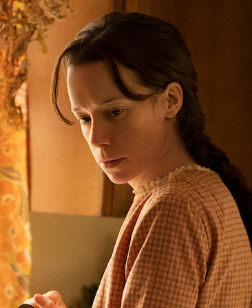 Chloe Pirrie headshot wearing an orange plaid shirt standing in a kitchen
