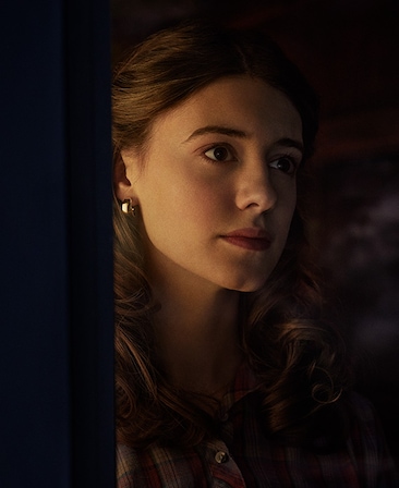 Daisy Edgar-Jones headshot wearing earrings standing behind a wall in the dark