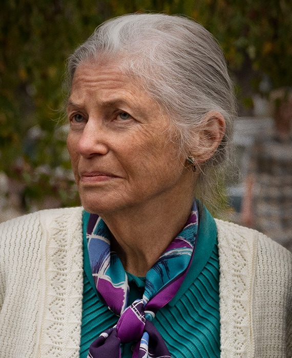 Sandra Seacat headshot wear a green top, white sweater and purple patterned scarf