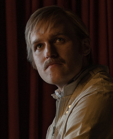 Wyatt Russell headshot wearing a beige jacket standing in the dark