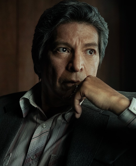 Gil Birmingham headshot wearing a striped shirt and placing his hand on his chin