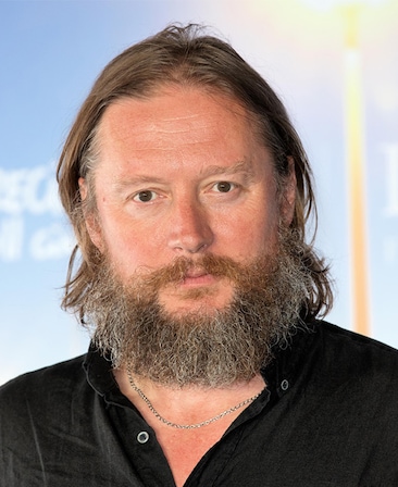 David Mackenzie headshot wearing a silver necklace and black top