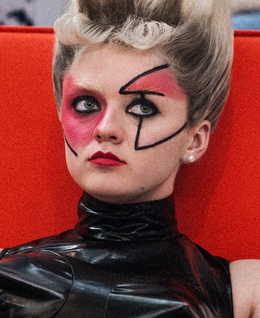 Maisie Williams headshot wearing a black leather top and red face make up
