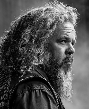 Mark Boonie headshot of his side profile with long hair and beard
