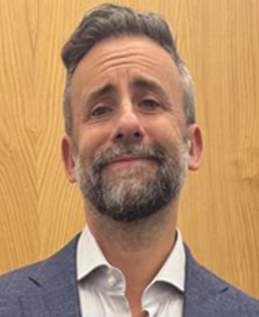 Headshot of executive producer Scott Marder wearing a blue suit and white button up, posing in front of a wooden wall.