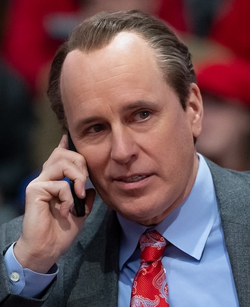 Andy Posner as Kelly AuCoin in FX's Clipped wearing a suit with a bright red tie, while on the phone.