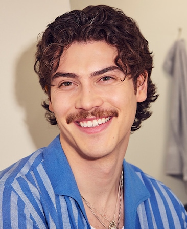 Headshot of Jack Innanen as Paul Baker in FX's Adults, wearing a blue striped button down shirt and necklace tucked under.