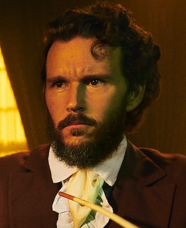 Ryan Kwanten headshot in plantation style brown suit with white neck tie scarf, with long yellow pipe hanging across chest