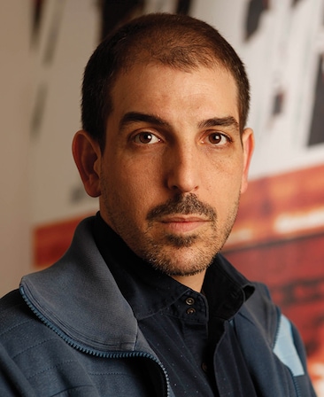 Glenn Kessler headshot in blue jacket and blue button down with red and white graphic image background