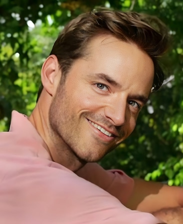 Headshot of executive producer Connor Hines of FX's Love Story, wearing a pink polo shirt with shrubbery behind.